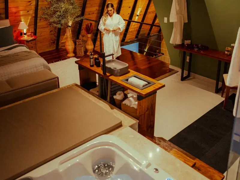 Sala de spa com mesas de massagem, iluminação aconchegante e um expositor de madeira com uma estátua reclinada sobre uma pequena mesa.