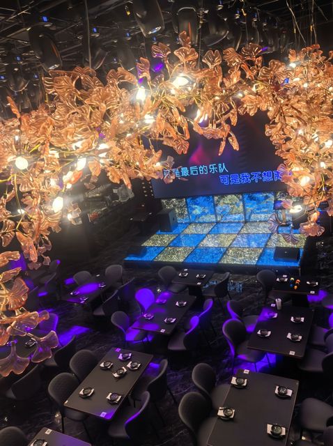 Dimly lit dining venue with ornate chandeliers and blue-lit tables set for guests