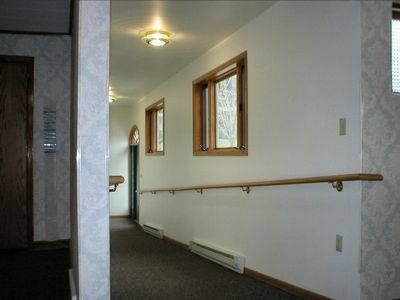 Hallway with white walls, wood trim, two windows, and a handrail.