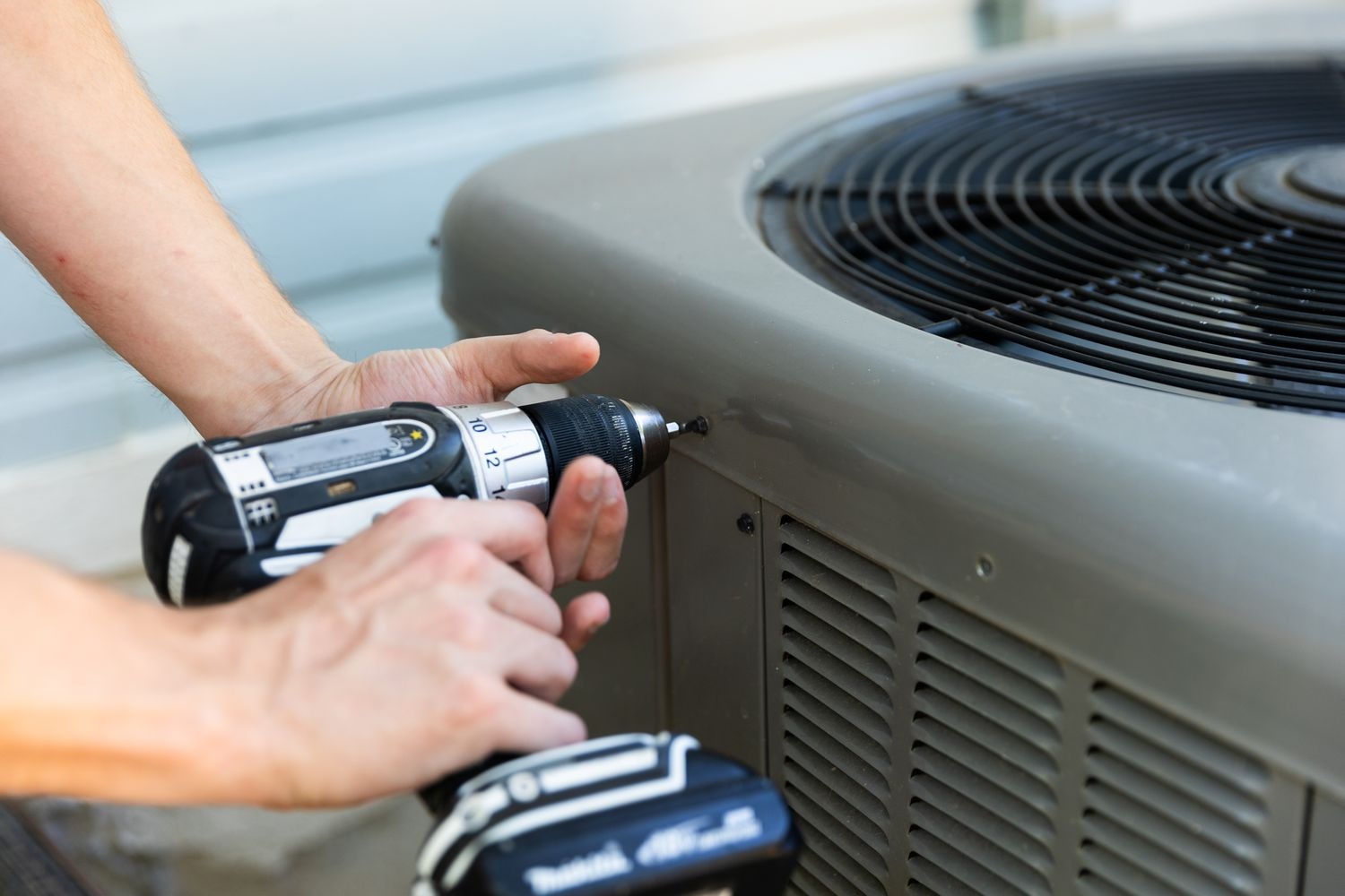 A man is using a drill to fix an air conditioner.