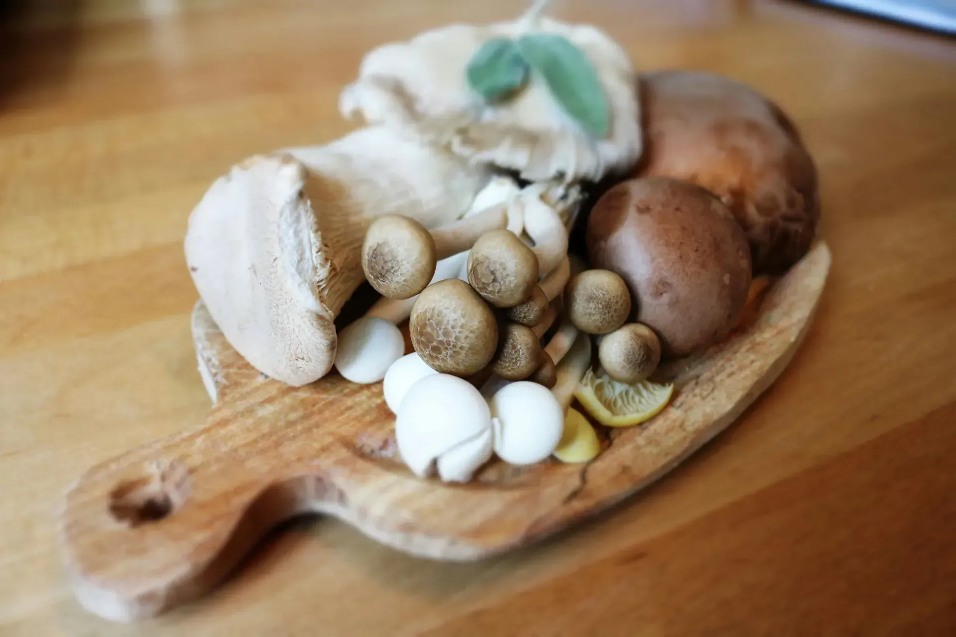Variety of mushrooms on a wooden cutting board, with a lemon slice and sage.