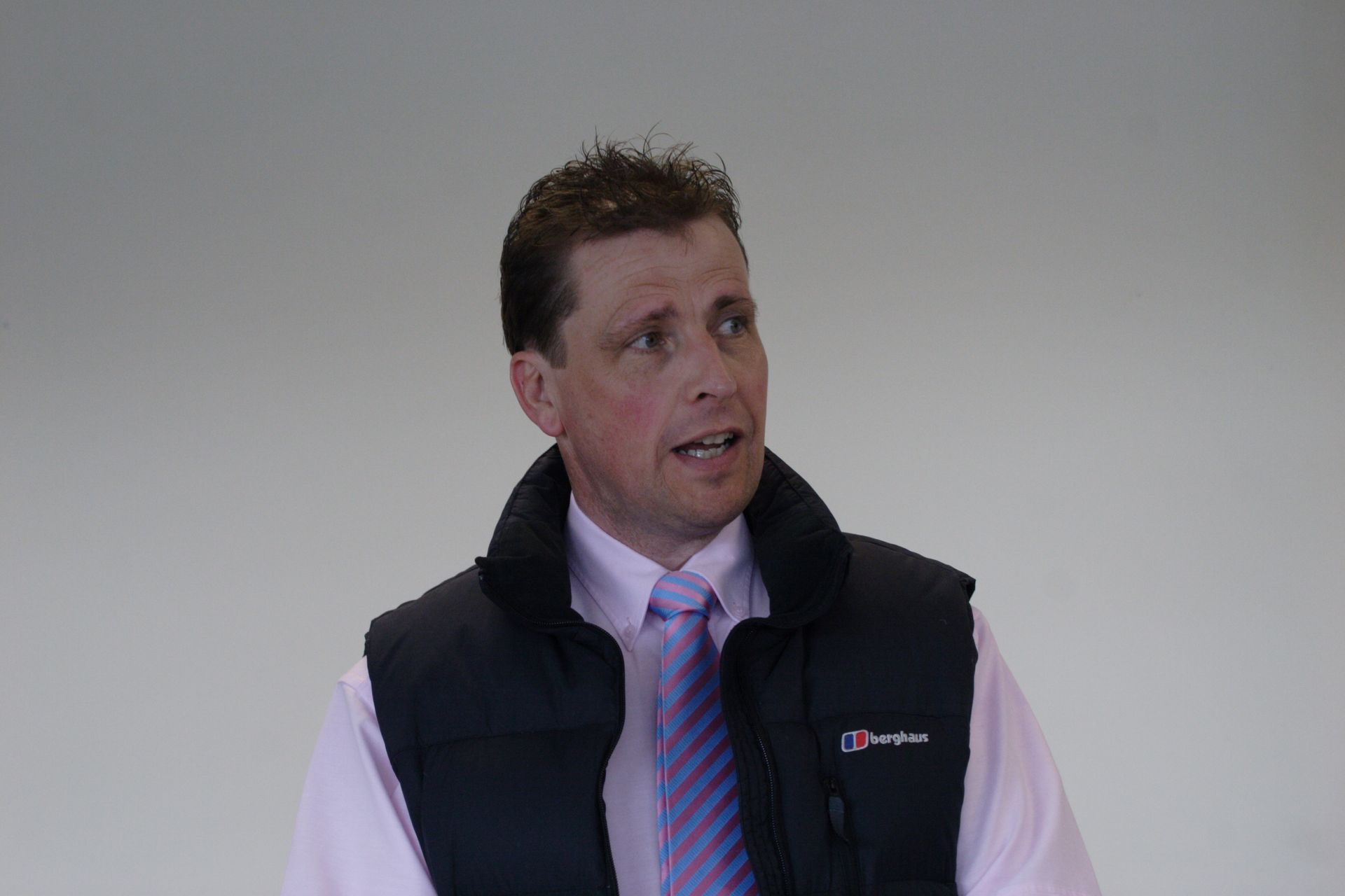 Man in black vest and tie looking up and to the left, set against a plain background.