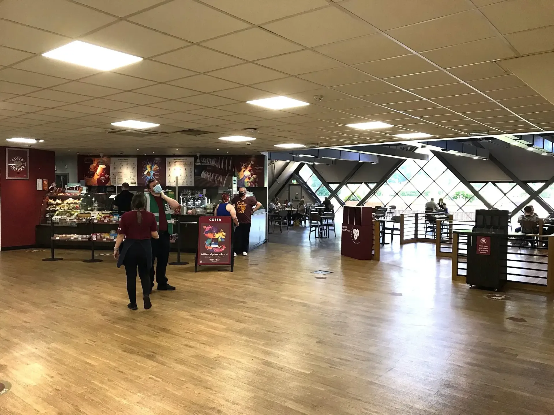 Interior shot of a cafe with people. Shop area on the left, geometric windowed seating area on the right.