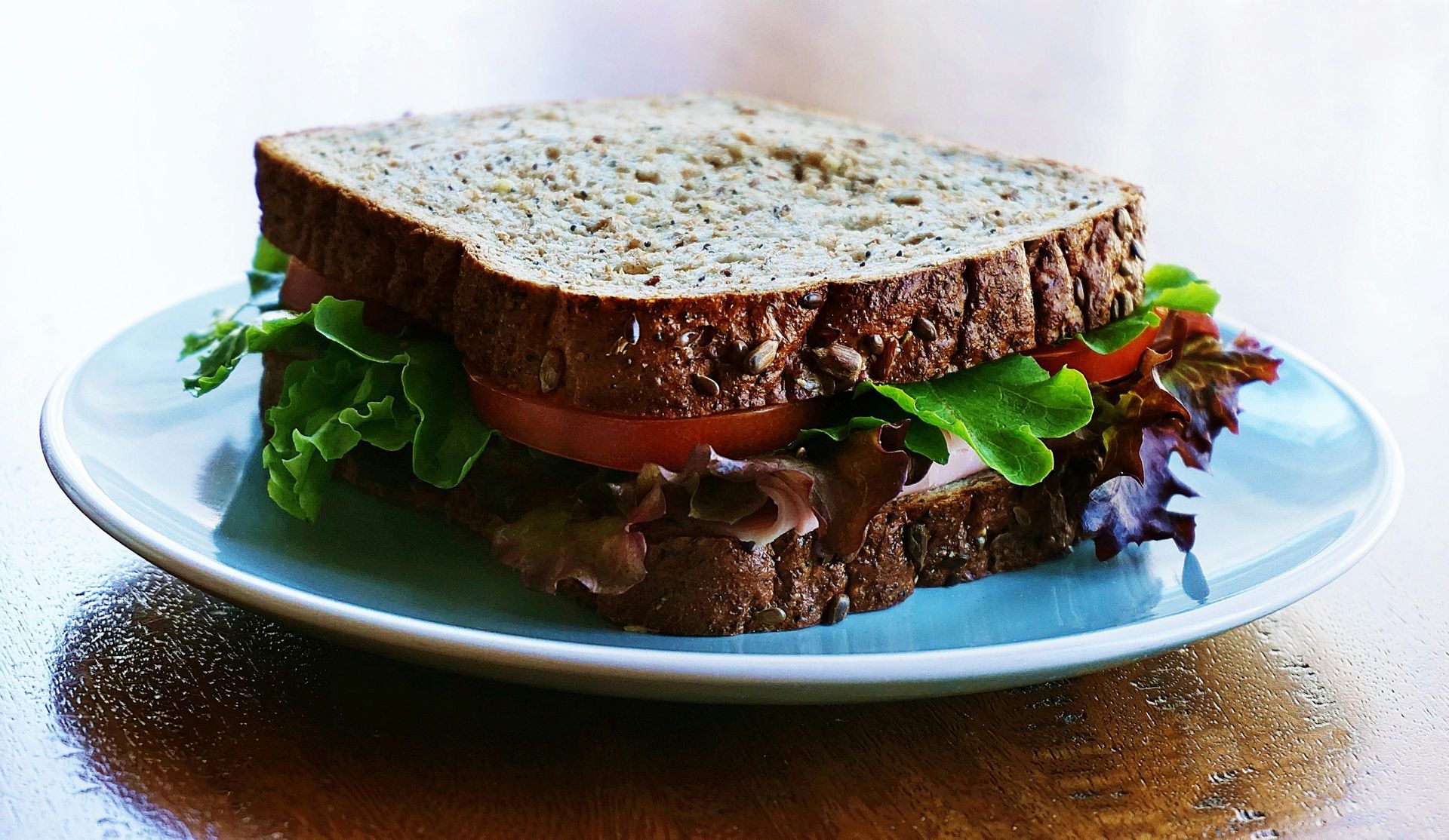 Sandwich on blue plate, wheat bread, with lettuce, tomato, and dark meat.