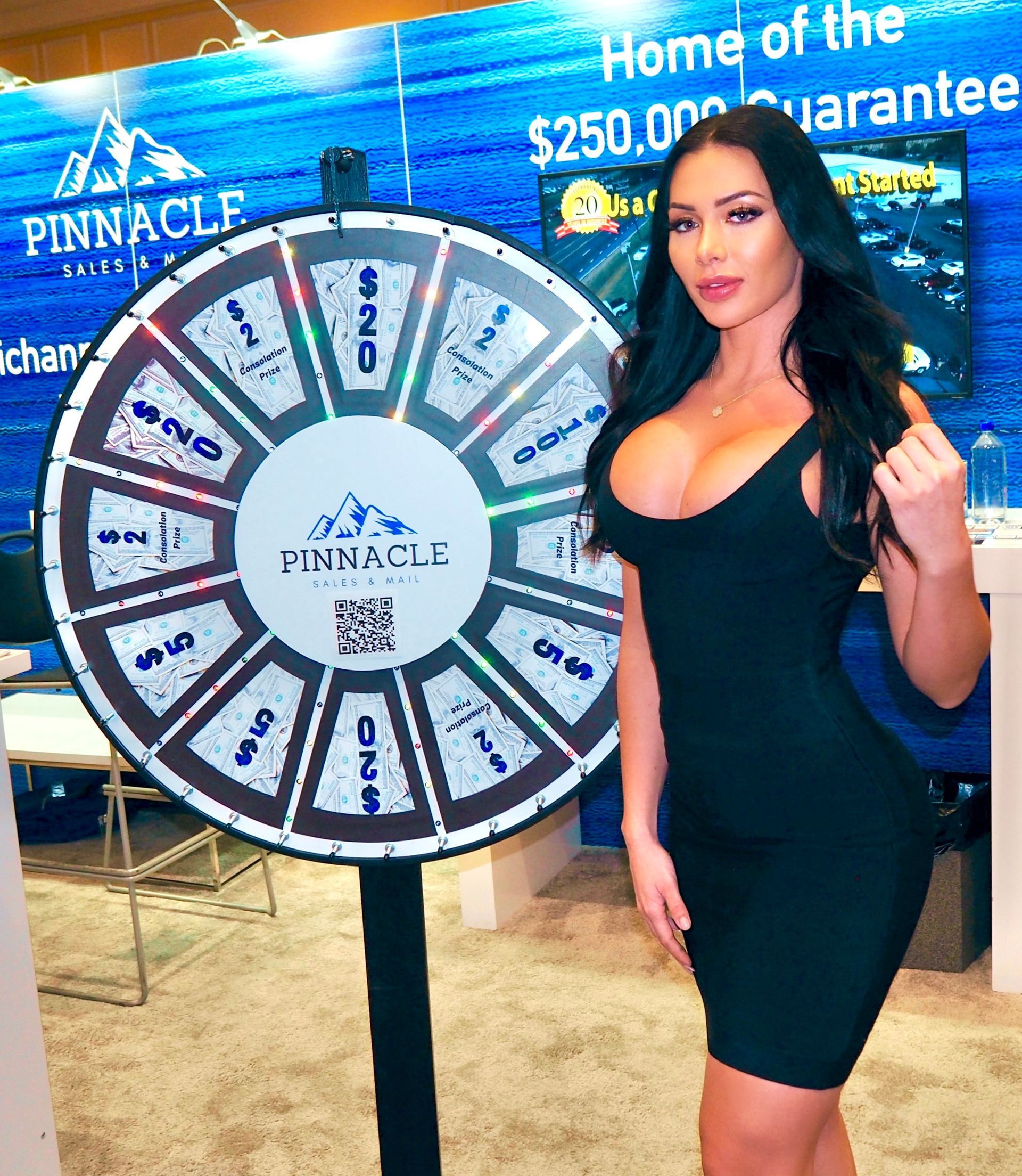Booth model at the Pinnacle Sales booth at the NADA Show in Las Vegas, standing beside a branded pin wheel display and engaging attendees on the trade show floor.