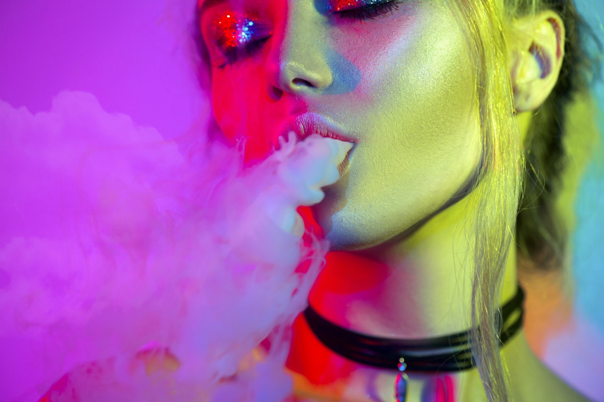 Woman exhales pink smoke, face illuminated by neon lights; wearing a choker.