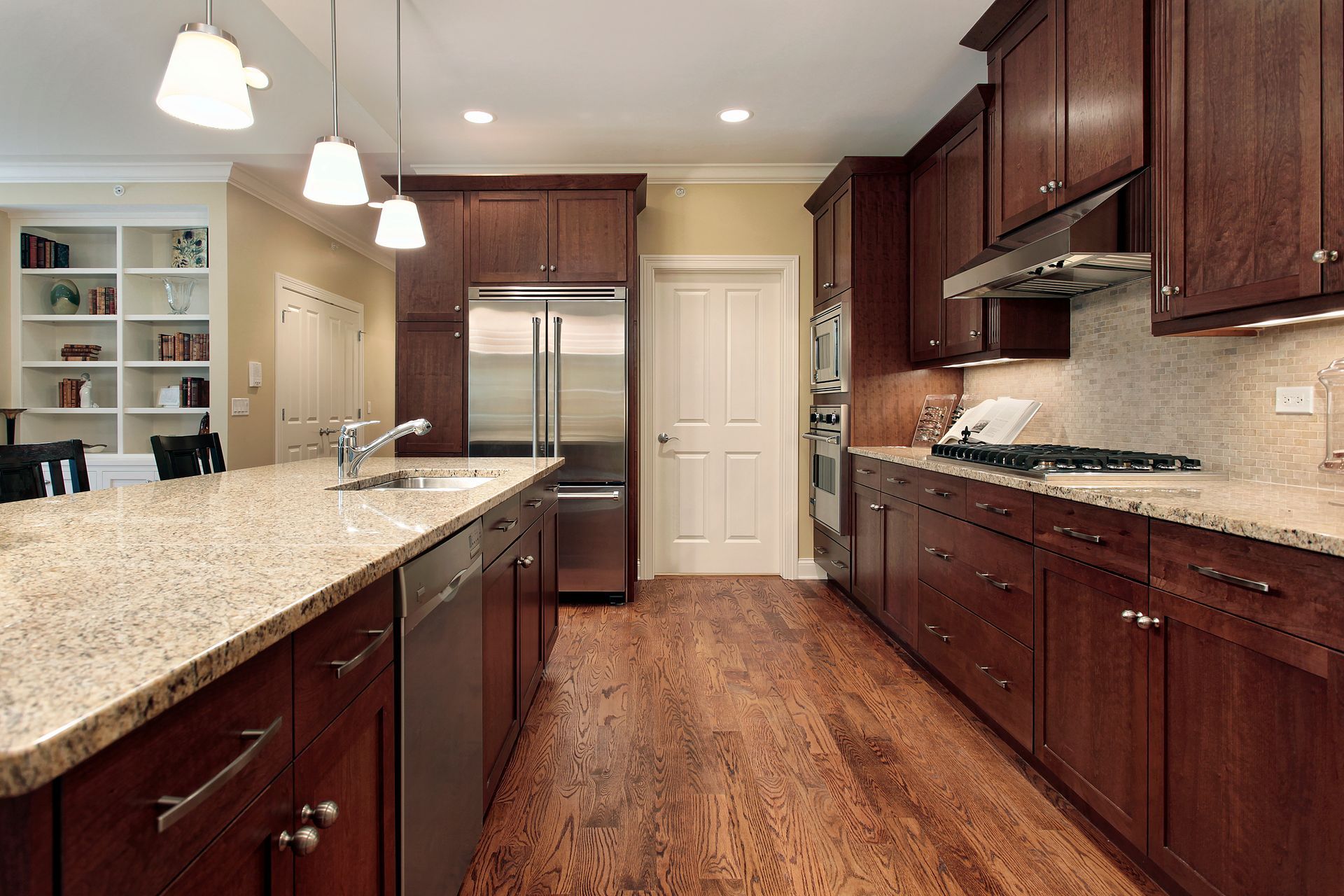 A well-lit kitchen with dark wooden cabinets, granite countertops, and stainless steel appliances.