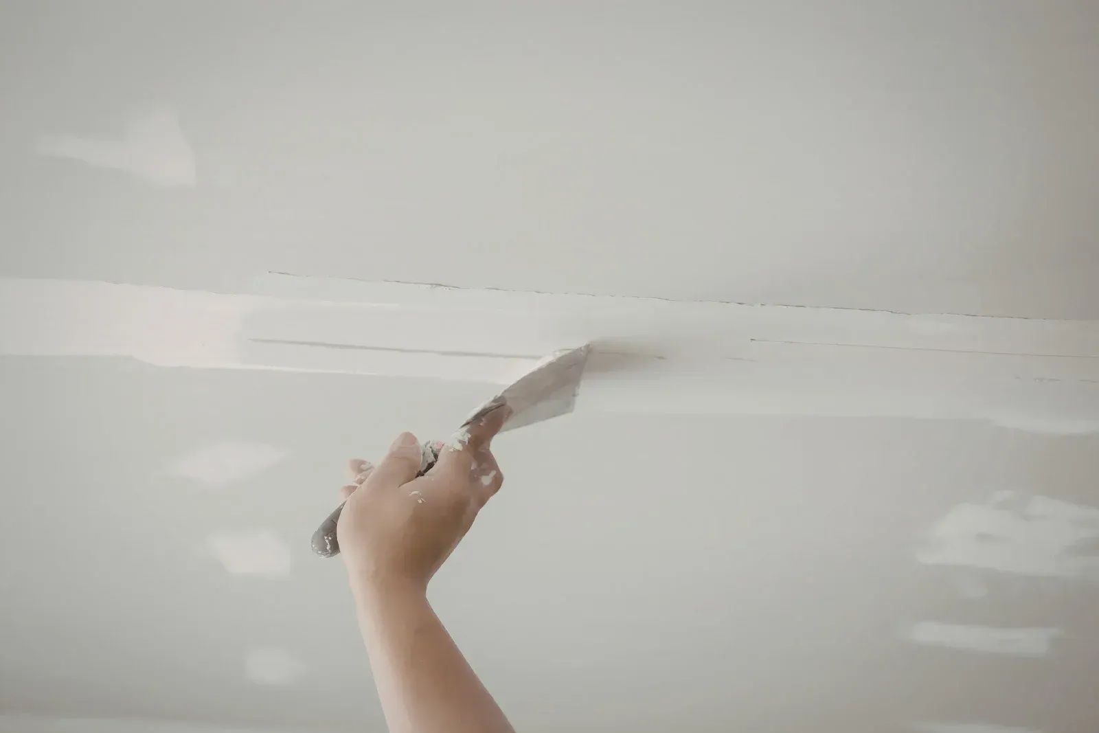 Person using a putty knife to apply joint compound to a seam on a white ceiling.