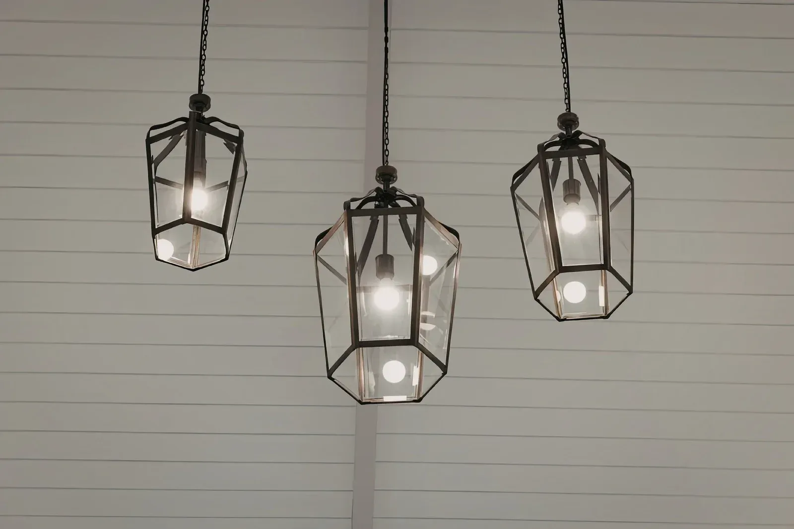 Three geometric pendant lights with visible bulbs hanging against a white horizontal-striped wall.