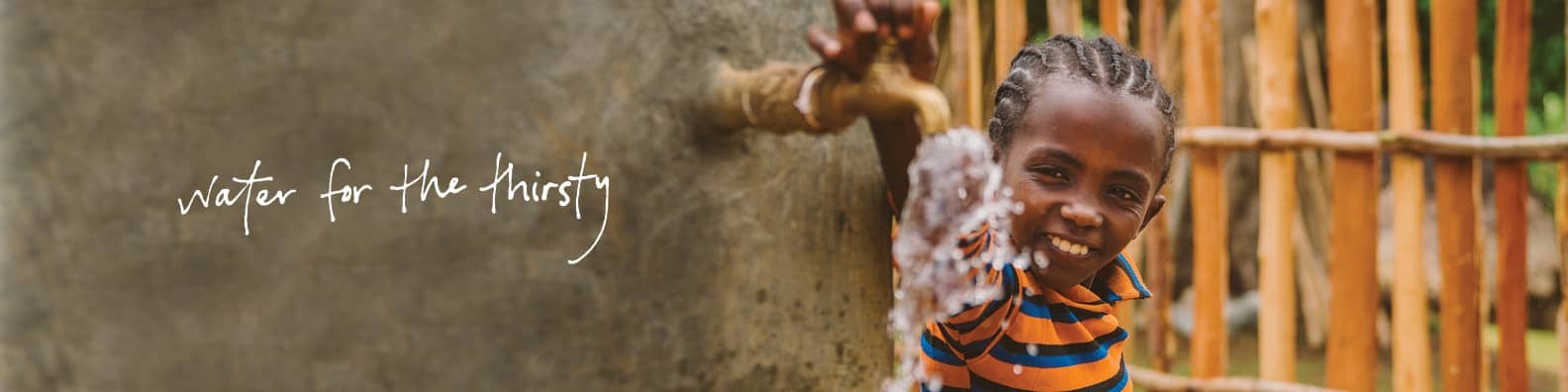 A young boy is drinking water from a faucet and smiling.