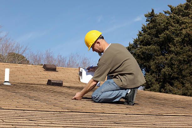 A man wearing a hard hat is kneeling on a roof.