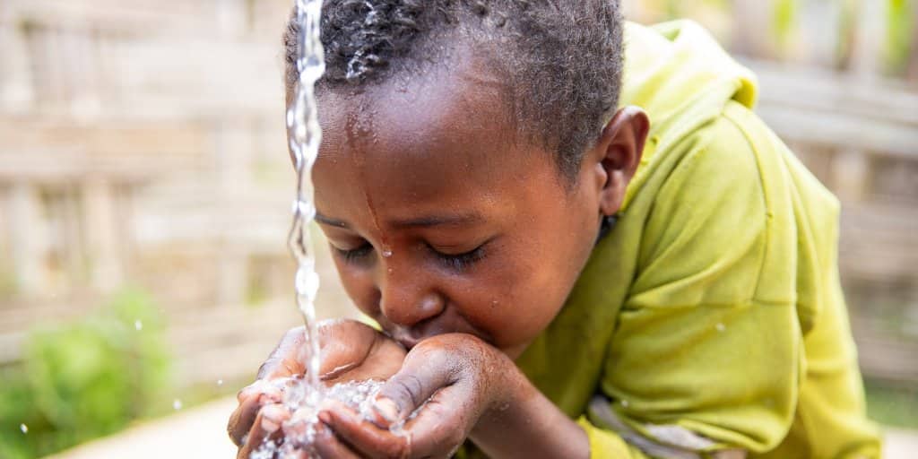 A young boy is drinking water from a fountain.
