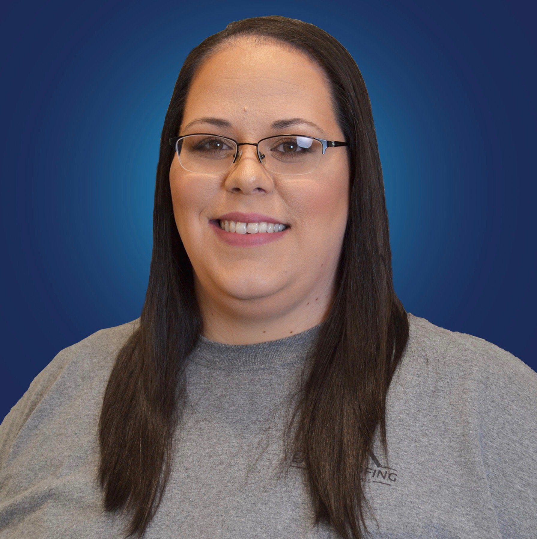 A woman wearing glasses and a grey shirt is smiling for the camera.