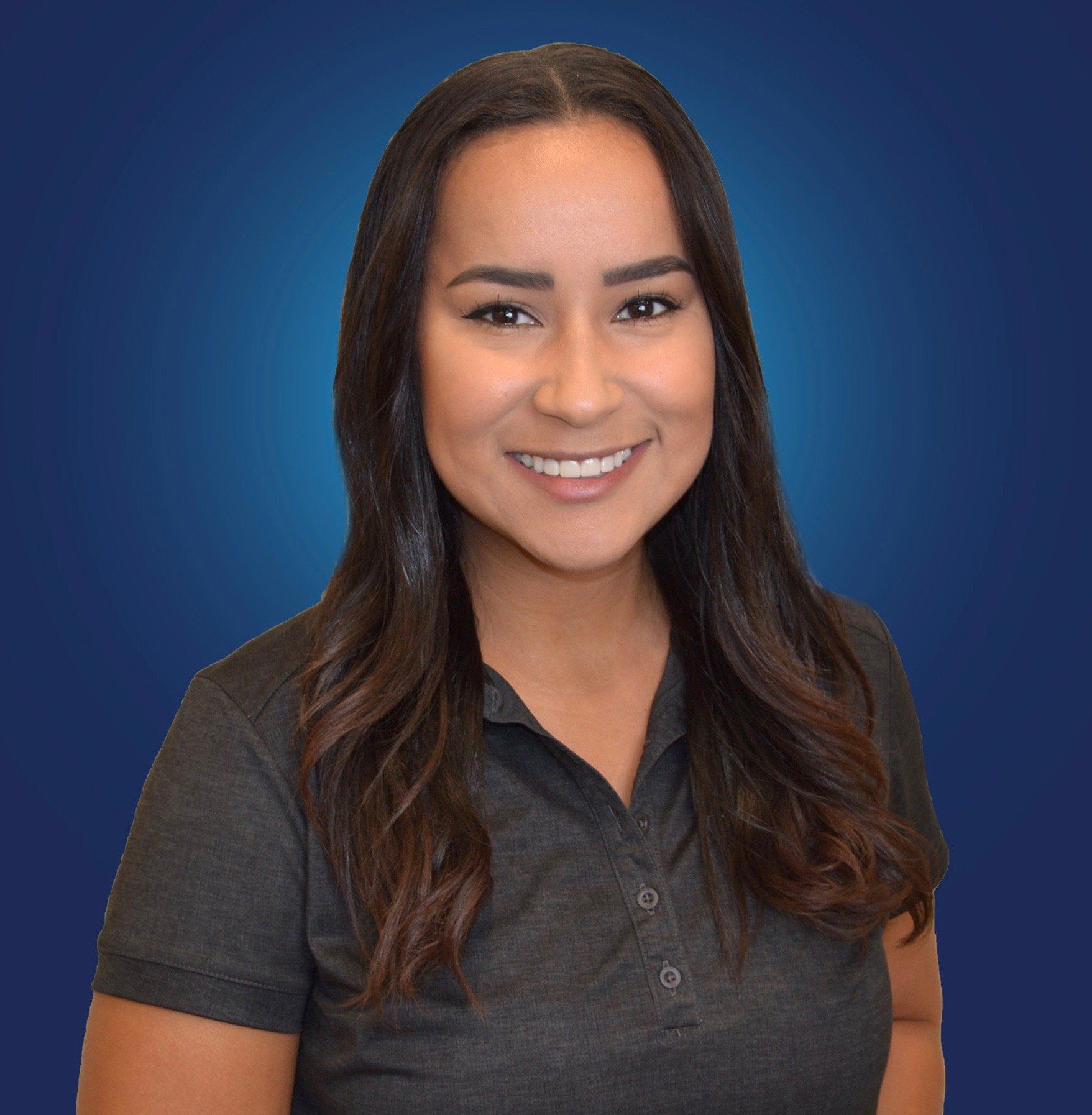 A woman in a gray shirt is smiling in front of a blue background.