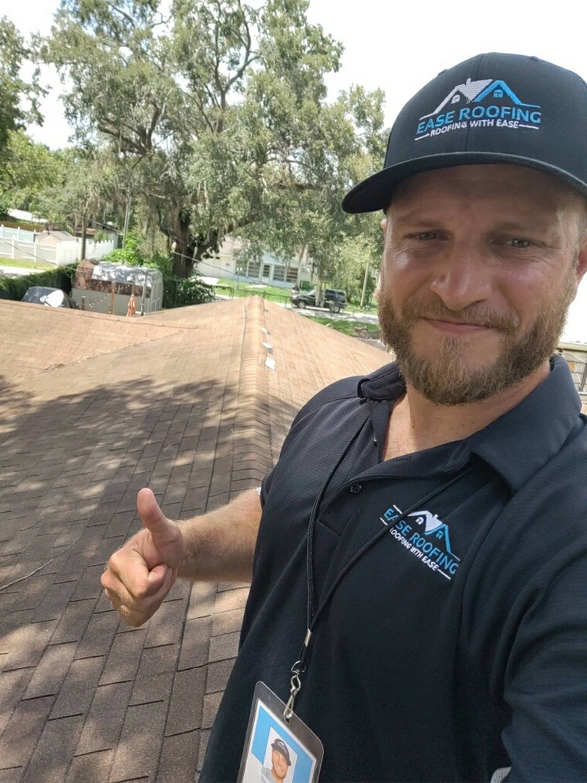 A man wearing a hat is giving a thumbs up while standing on a roof.