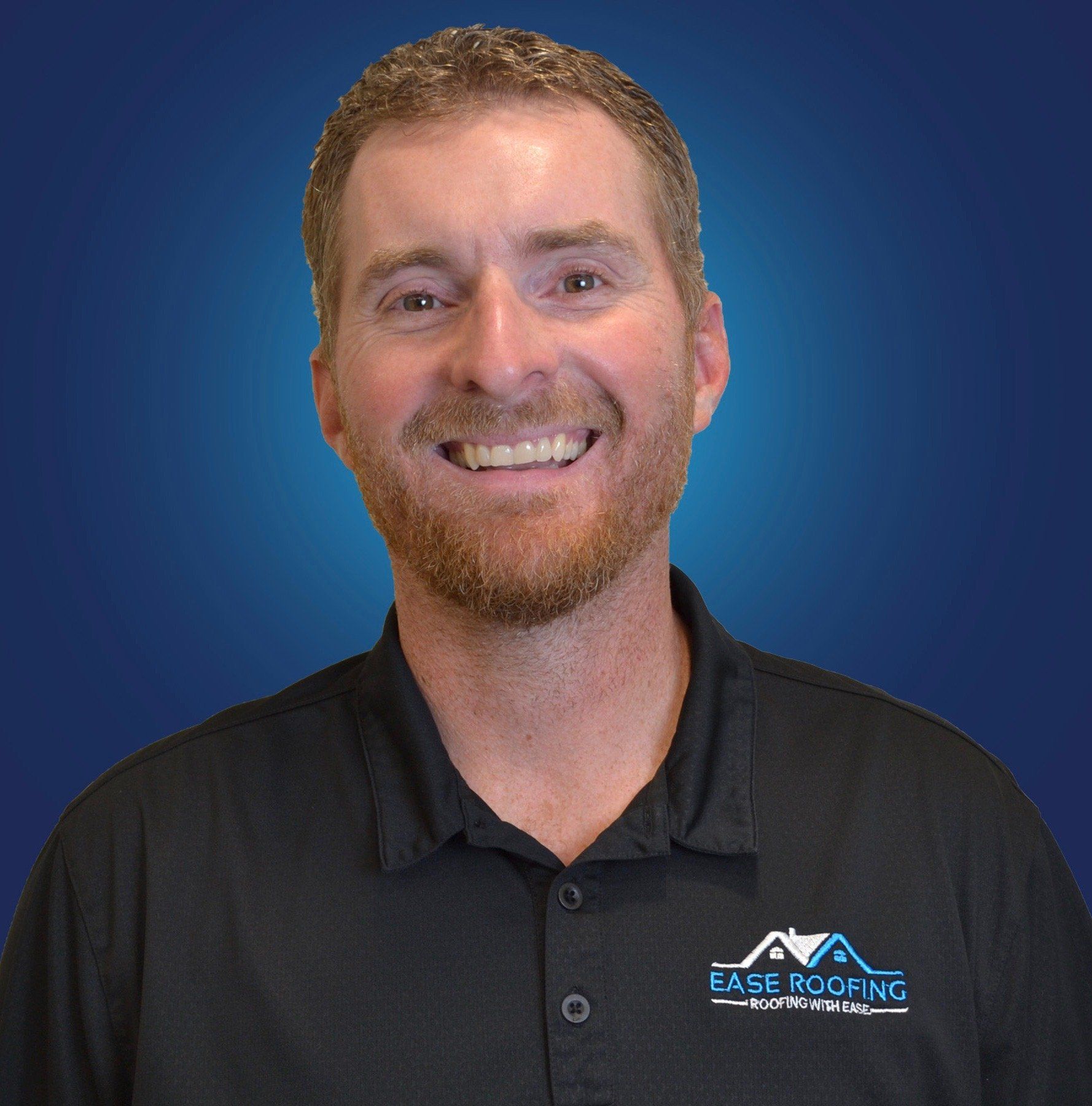 A man with a beard is wearing a black polo shirt and smiling.