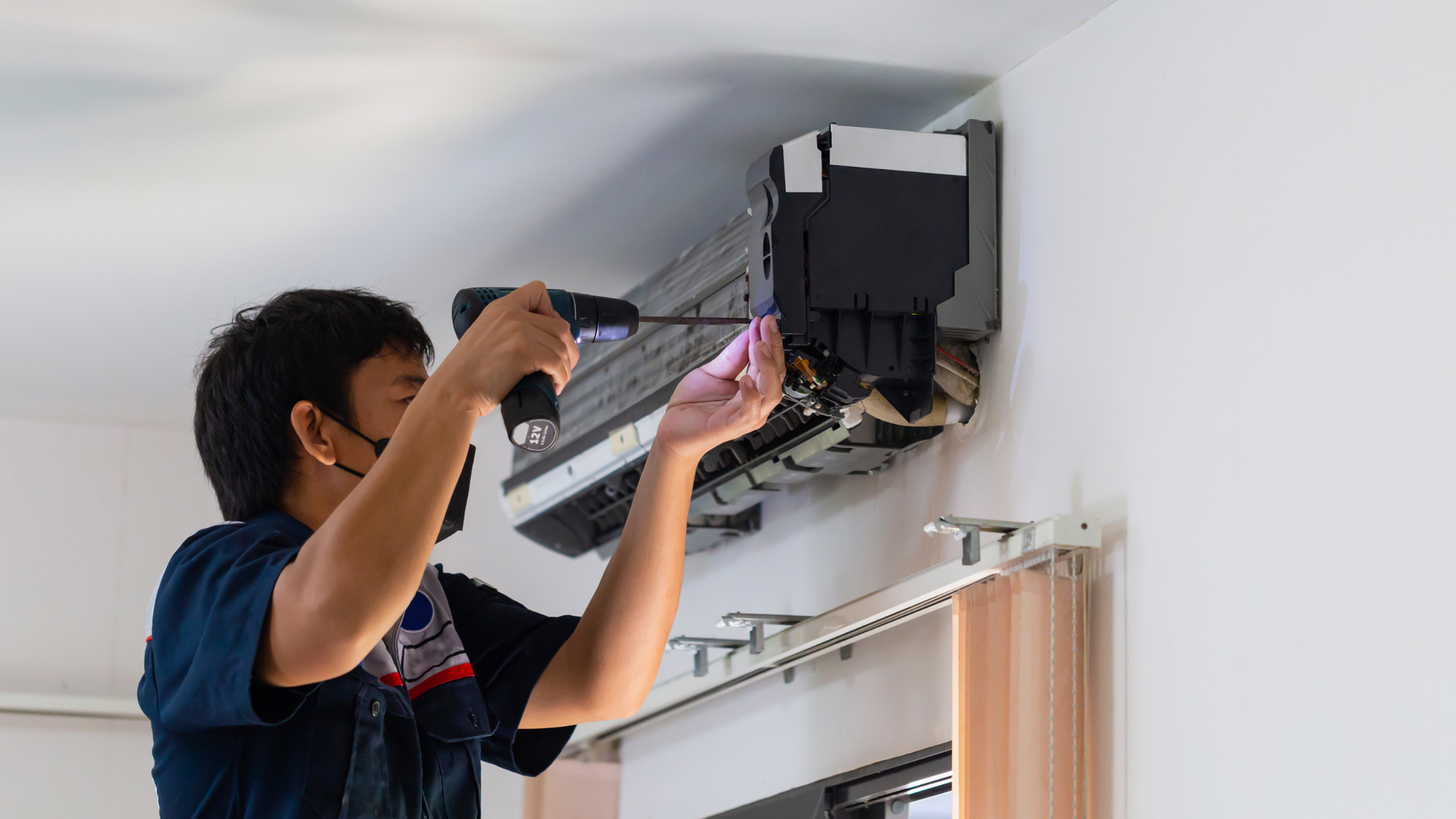 A man is fixing an air conditioner with a drill.