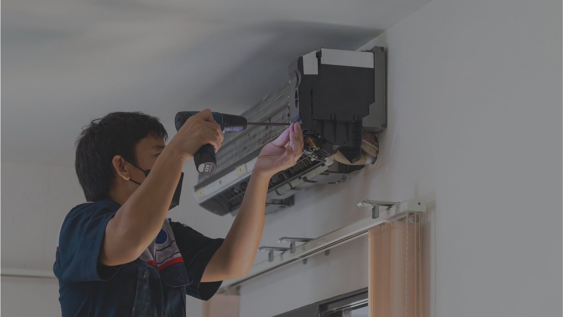 A man is using a drill to fix an air conditioner on the wall.