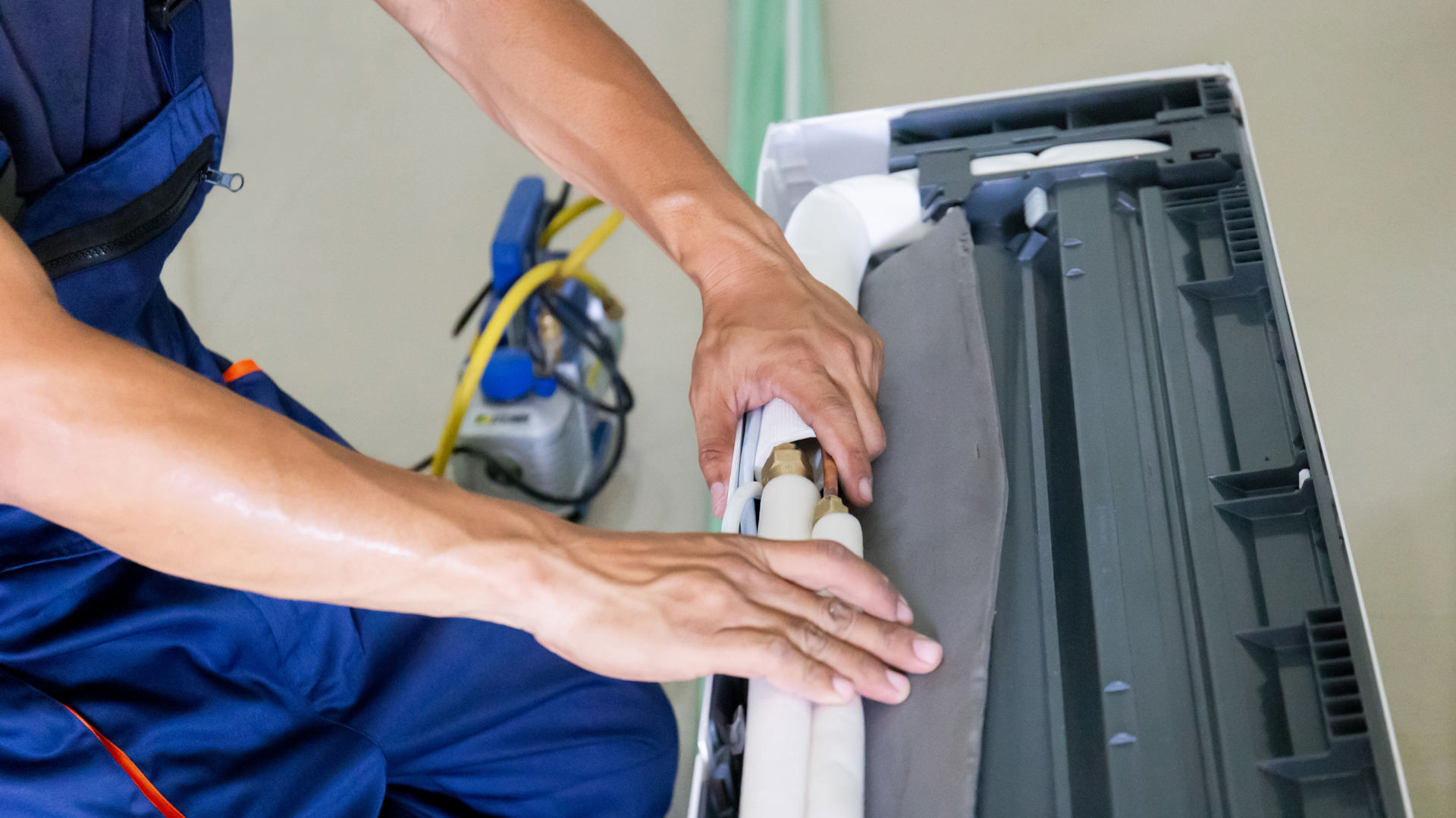 A man is sitting on the floor fixing an air conditioner.