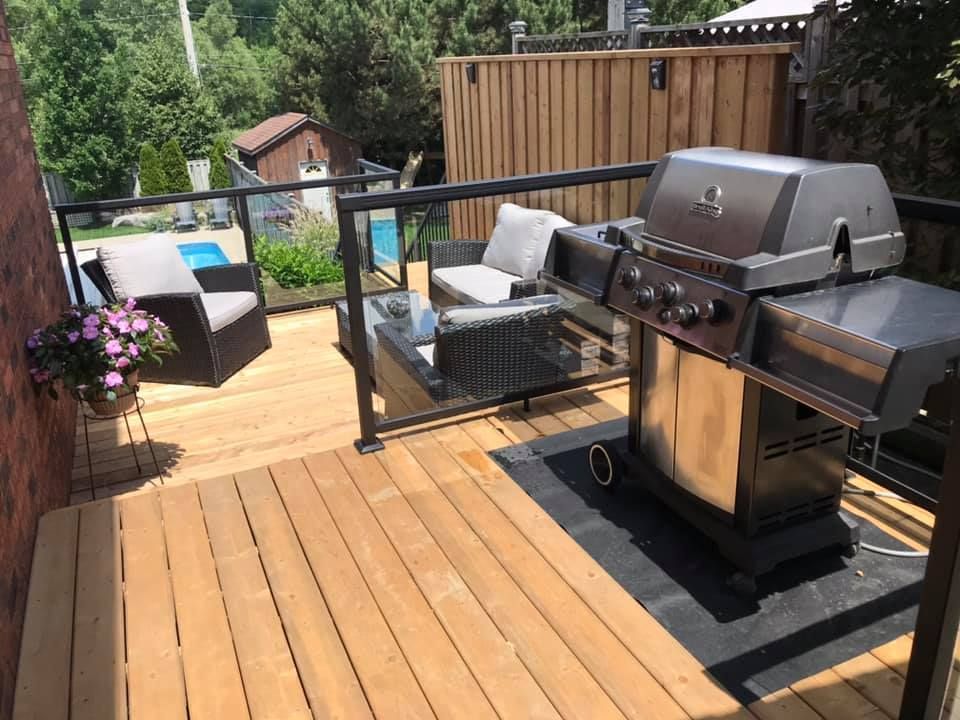 A backyard deck with a grill, seating area, and glass railing.