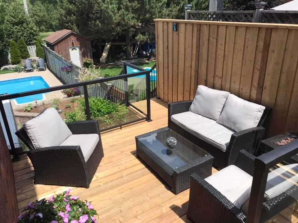 Outdoor deck with wicker furniture, overlooking a pool and yard, with wooden fence.