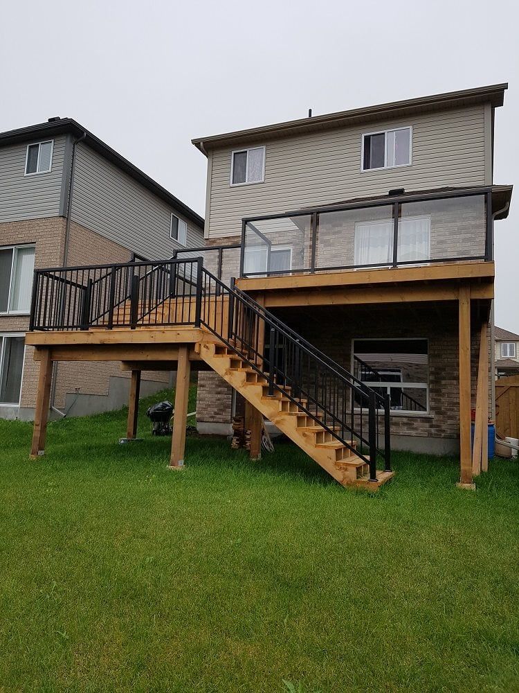 Backyard deck with wooden steps and black railings. House exterior in background.