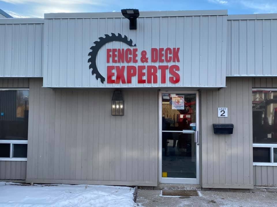 Fence & Deck Experts storefront with a saw blade logo, red text, and door number 2.