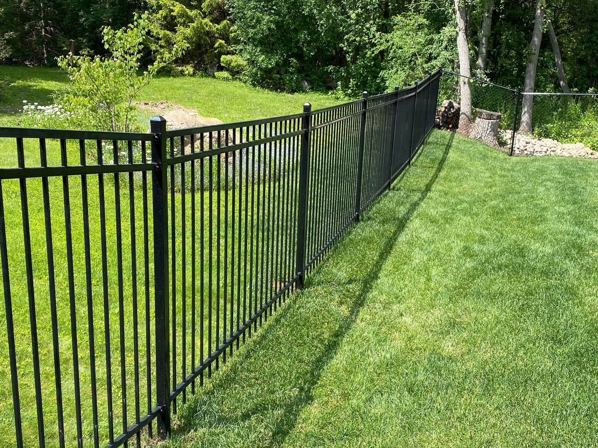 Black metal fence along a green lawn, with trees and bushes in the background.