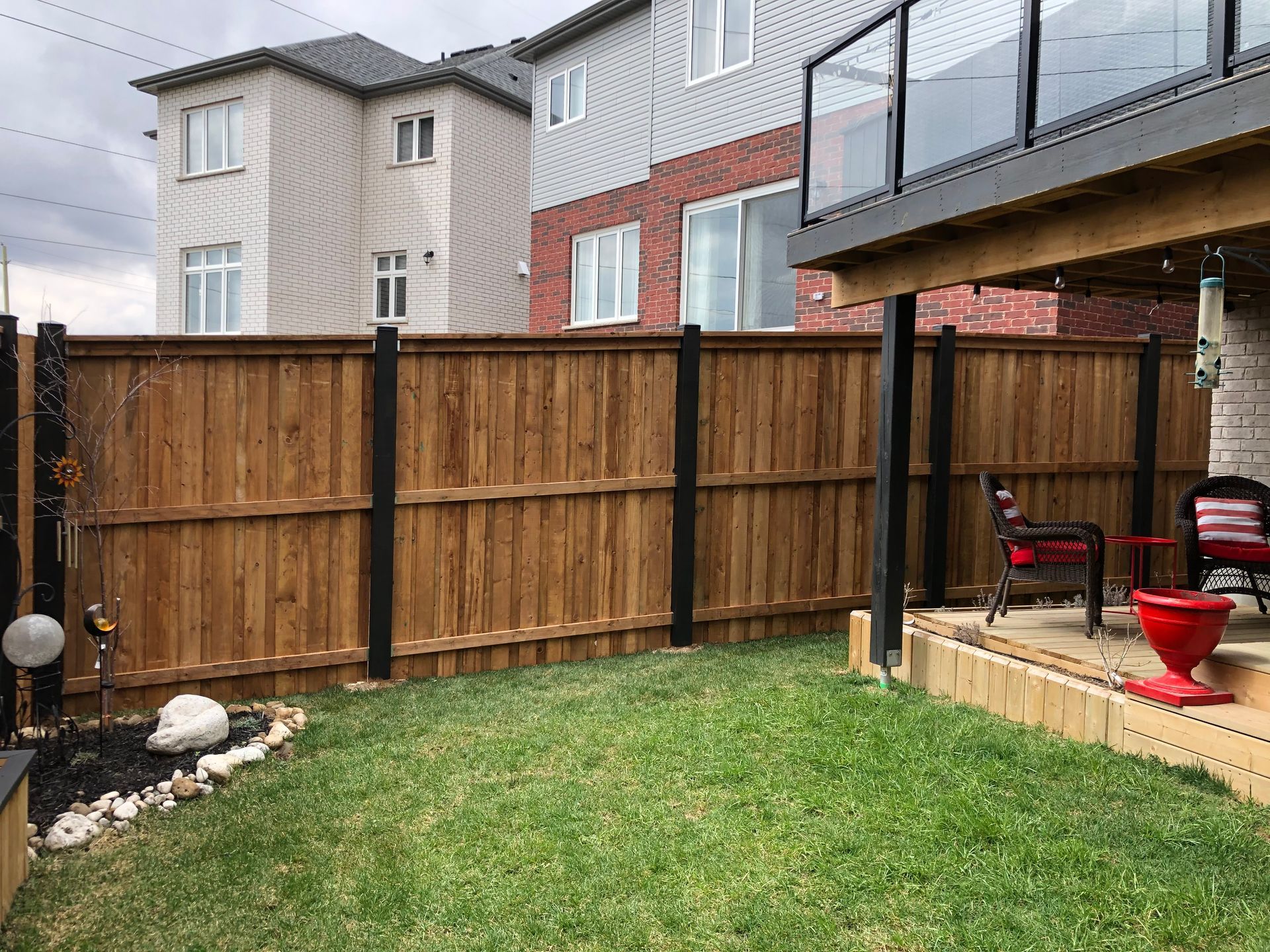 Wooden fence with black posts encloses a backyard with green grass and patio.