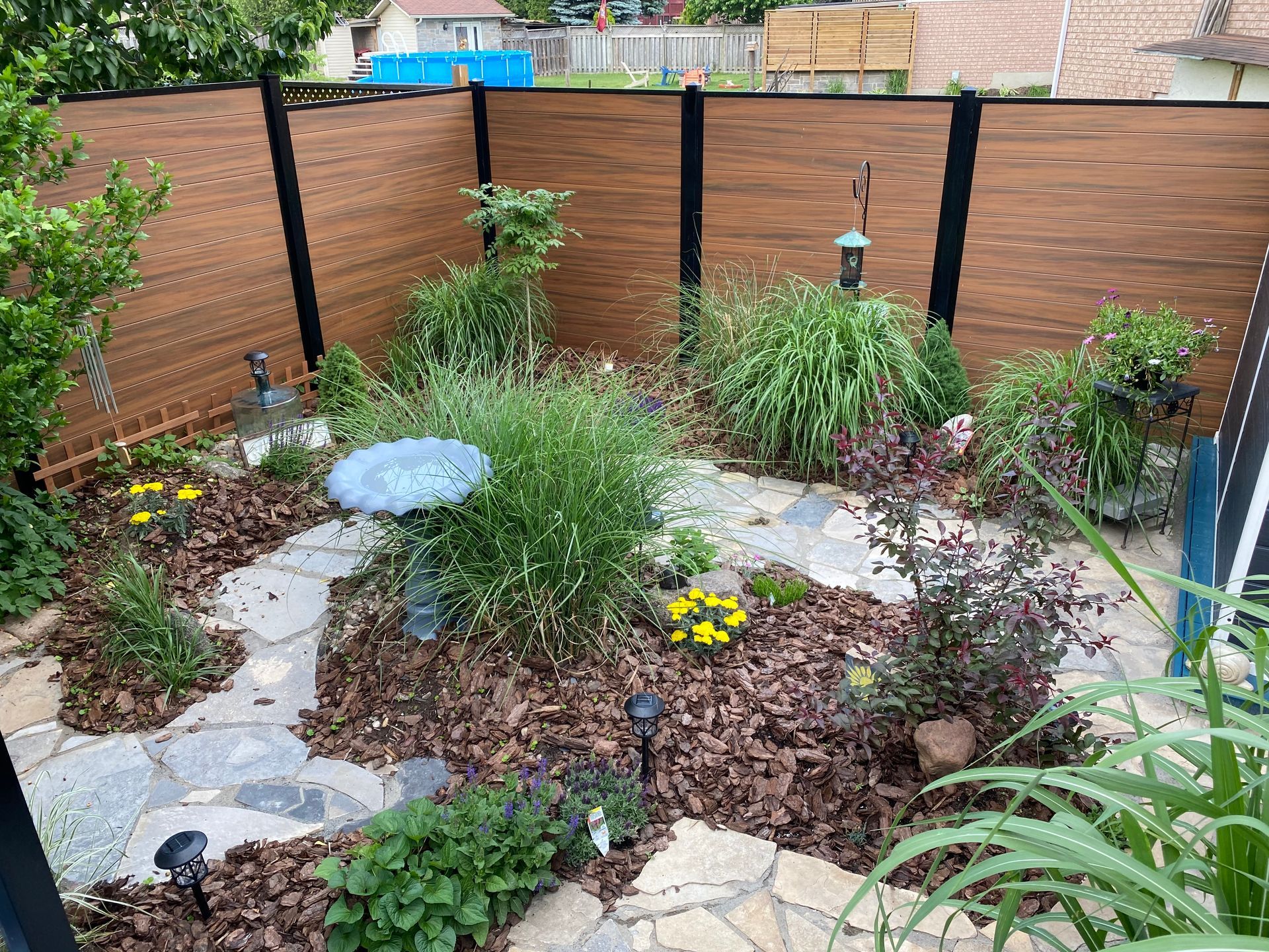 Backyard garden with flagstone path, bird bath, and wooden fence.