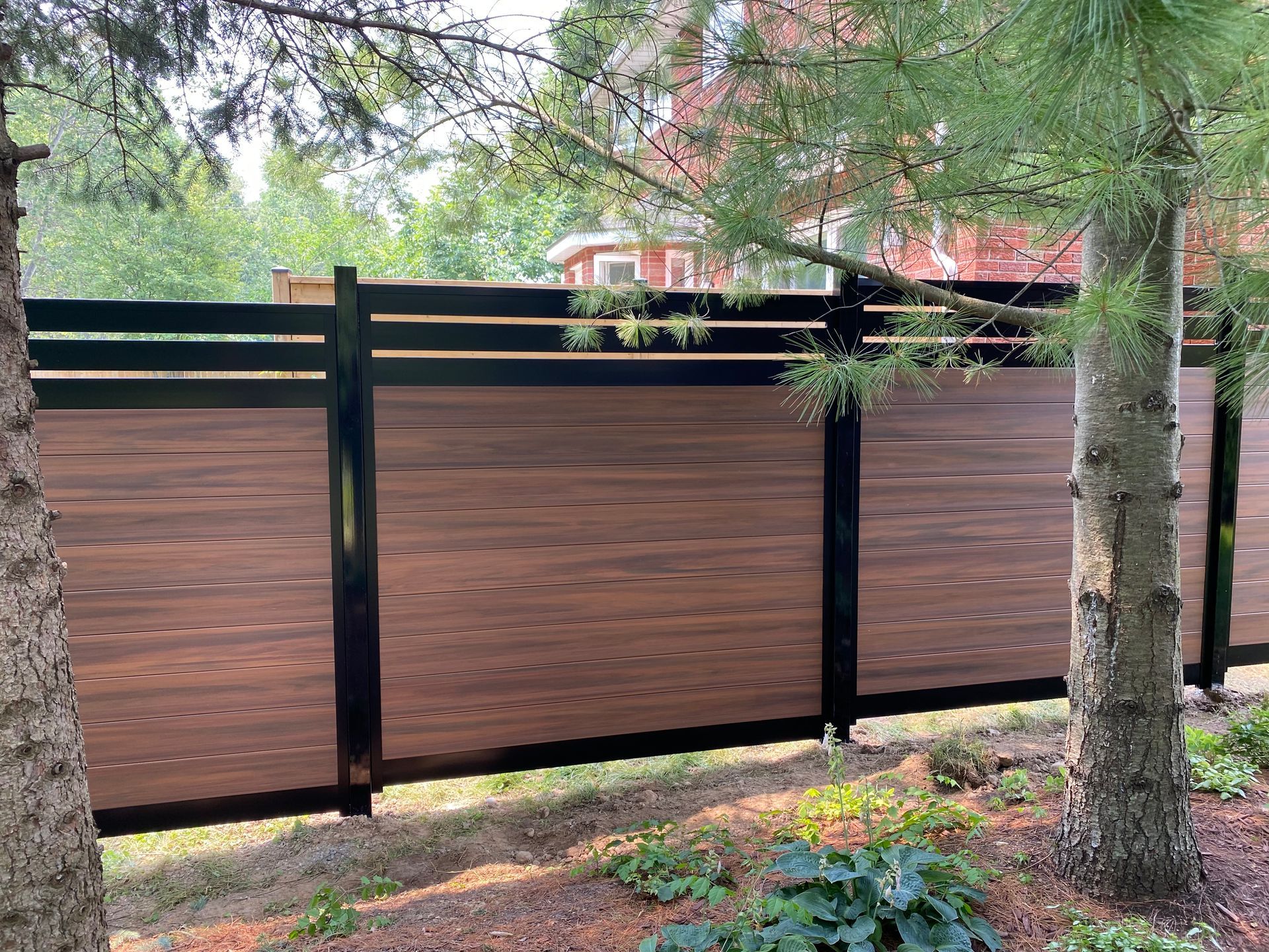 Brown and black horizontal privacy fence in a yard with trees.