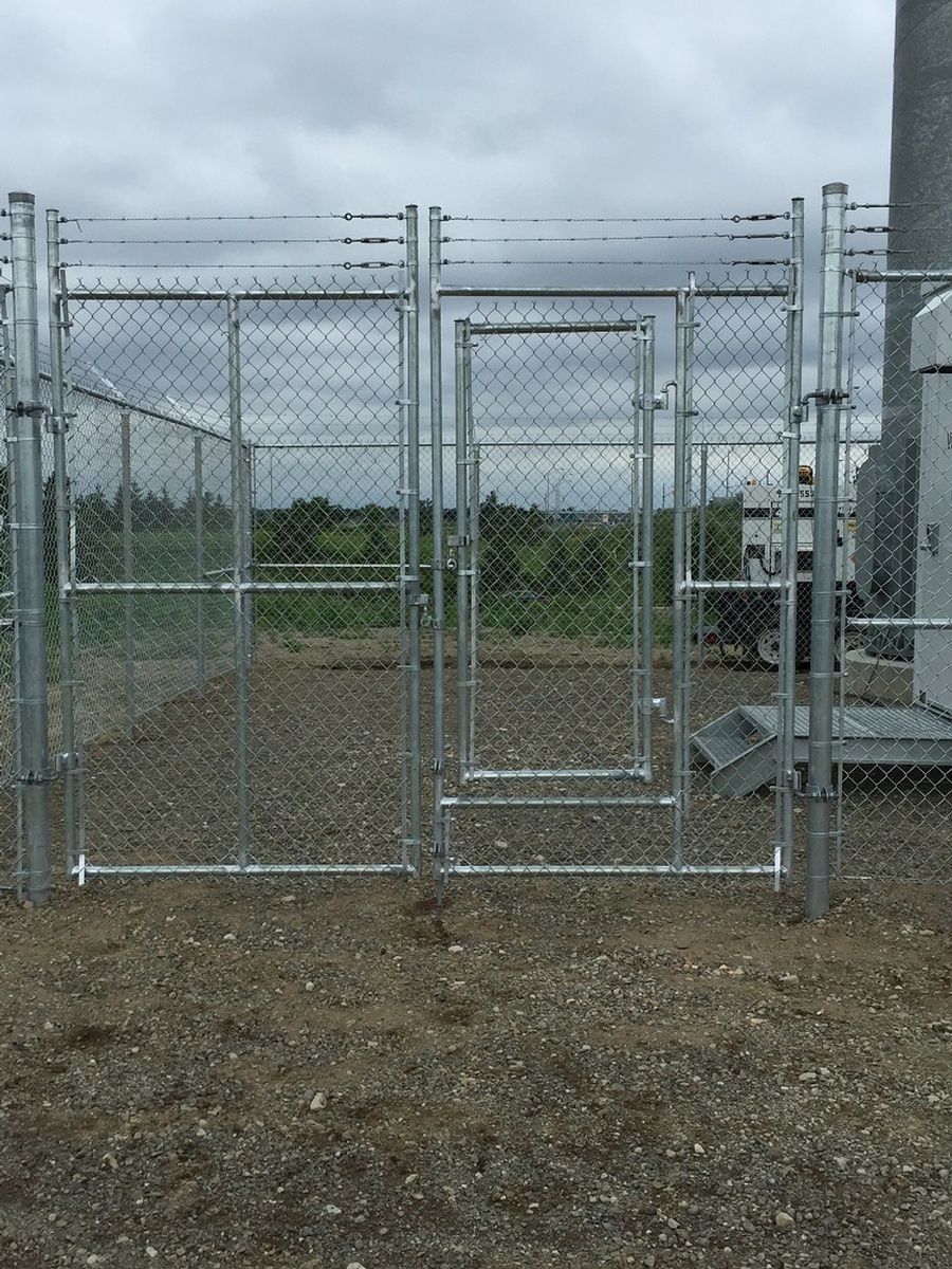 A fenced enclosure with multiple metal gates in a field, under an overcast sky.