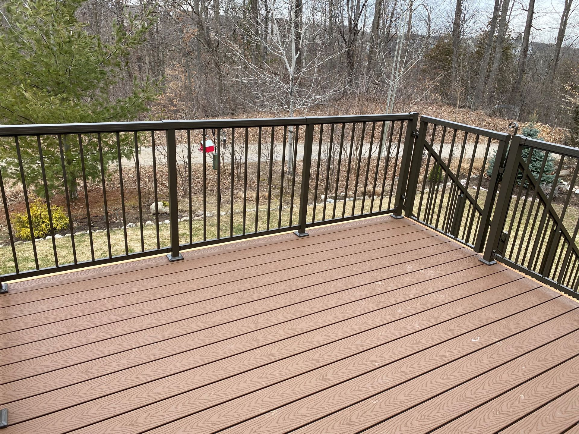 Brown composite deck with black railing overlooking trees.