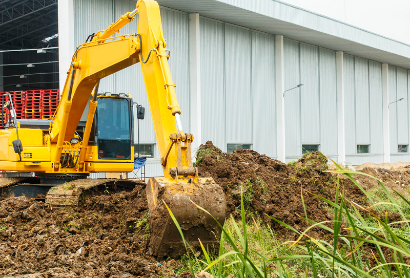 A yellow excavator is digging a pile of dirt in front of a building.