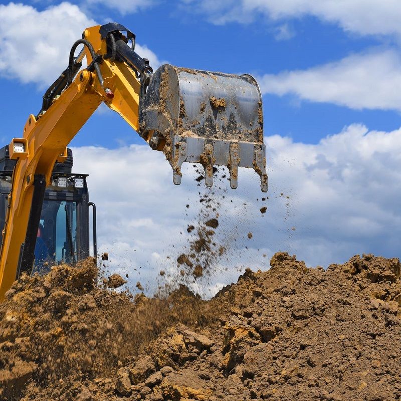 A yellow excavator is scooping dirt into a pile