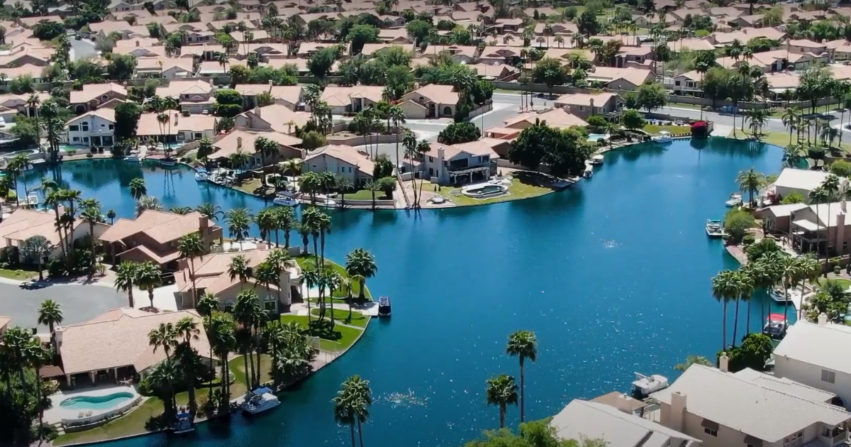 Aerial view of a suburban community with houses, waterways, and palm trees under a blue sky.