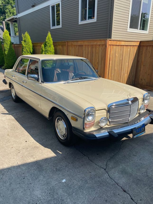 Beige classic sedan parked in a driveway beside a wooden fence and house.