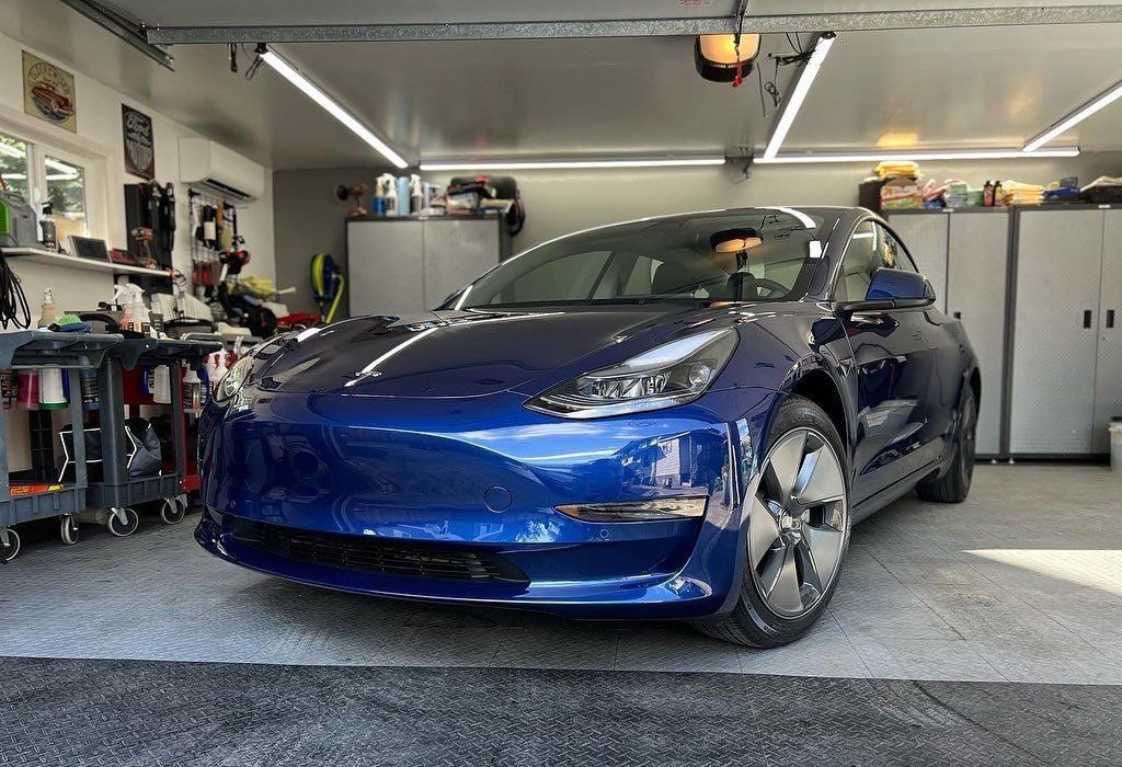 Blue Tesla electric car parked inside a well-lit garage.