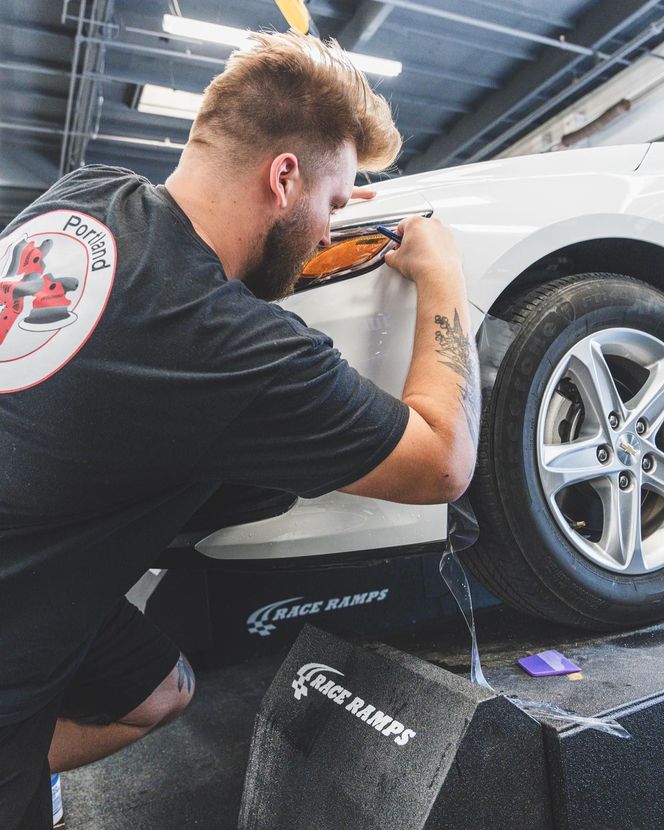 Mechanic polishing a white car’s wheel in a garage on a lift.