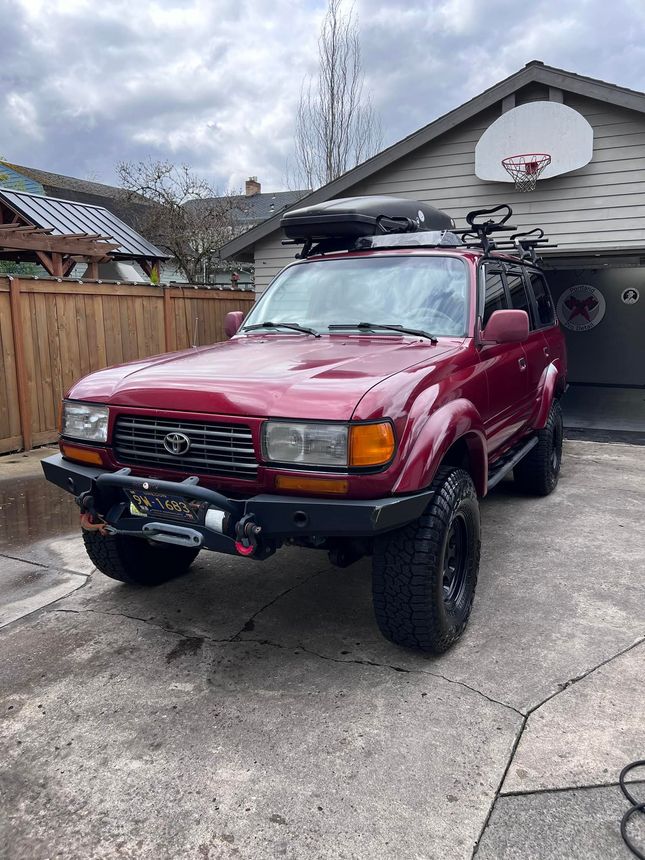 Red SUV parked in a driveway beside a garage, with a basketball hoop mounted above.