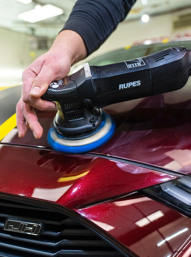 Person using a polisher on a red car hood in a garage