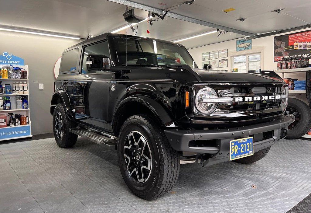 Black Ford Bronco parked inside a garage, with cleaning supplies and tools on display.