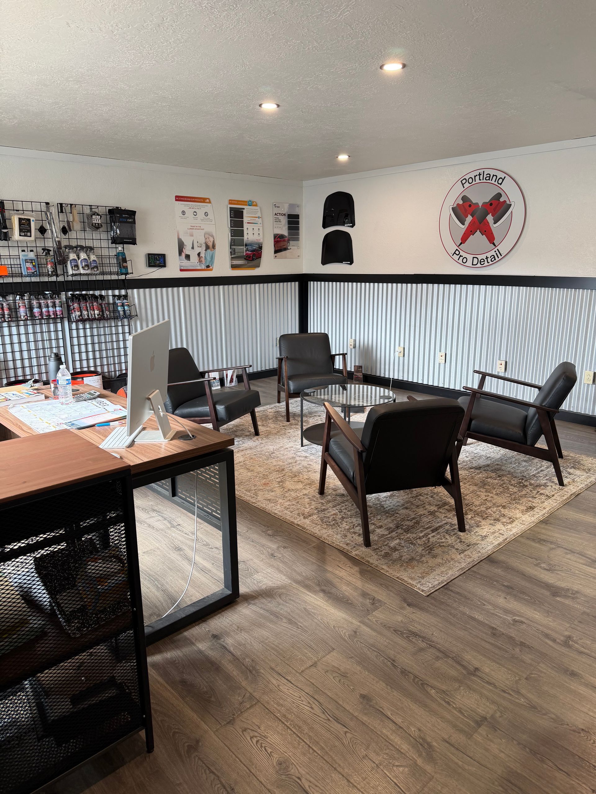 Modern lounge with black chairs, wood table, gray walls, and a patterned rug under recessed lights