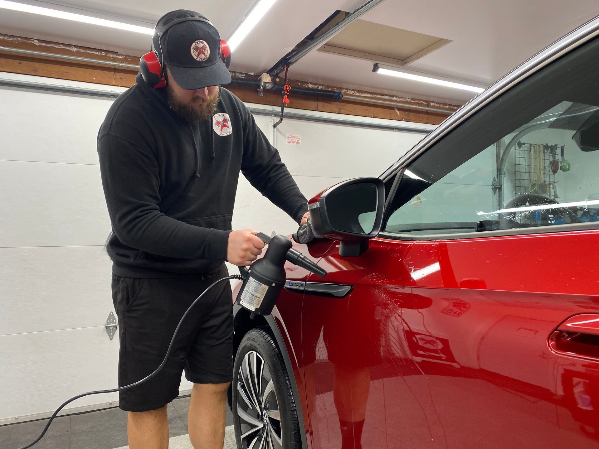 Man polishing a red car in a garage with an electric buffer