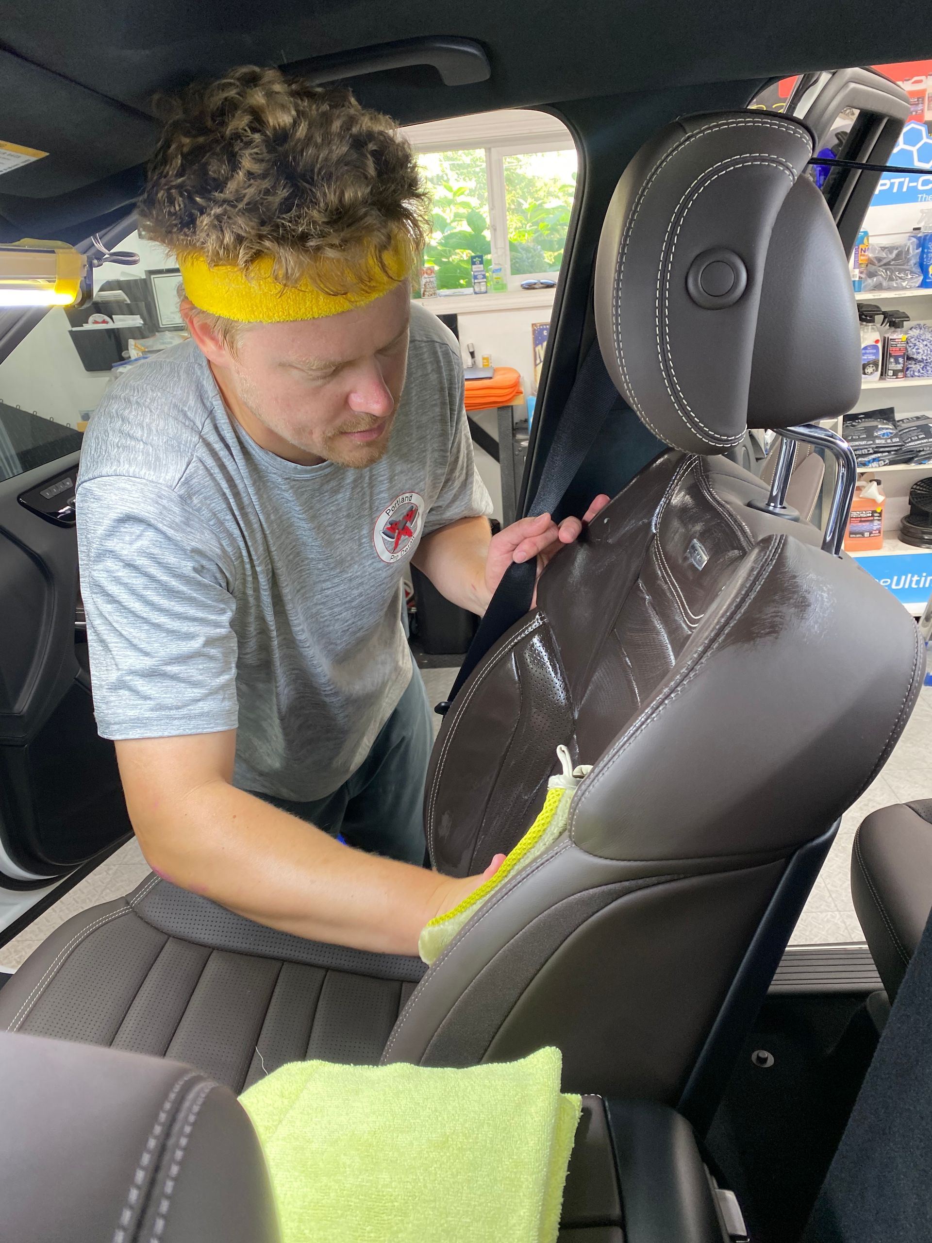 Person wiping the inside of a car seat, with a yellow headband and green cloth in a car interior