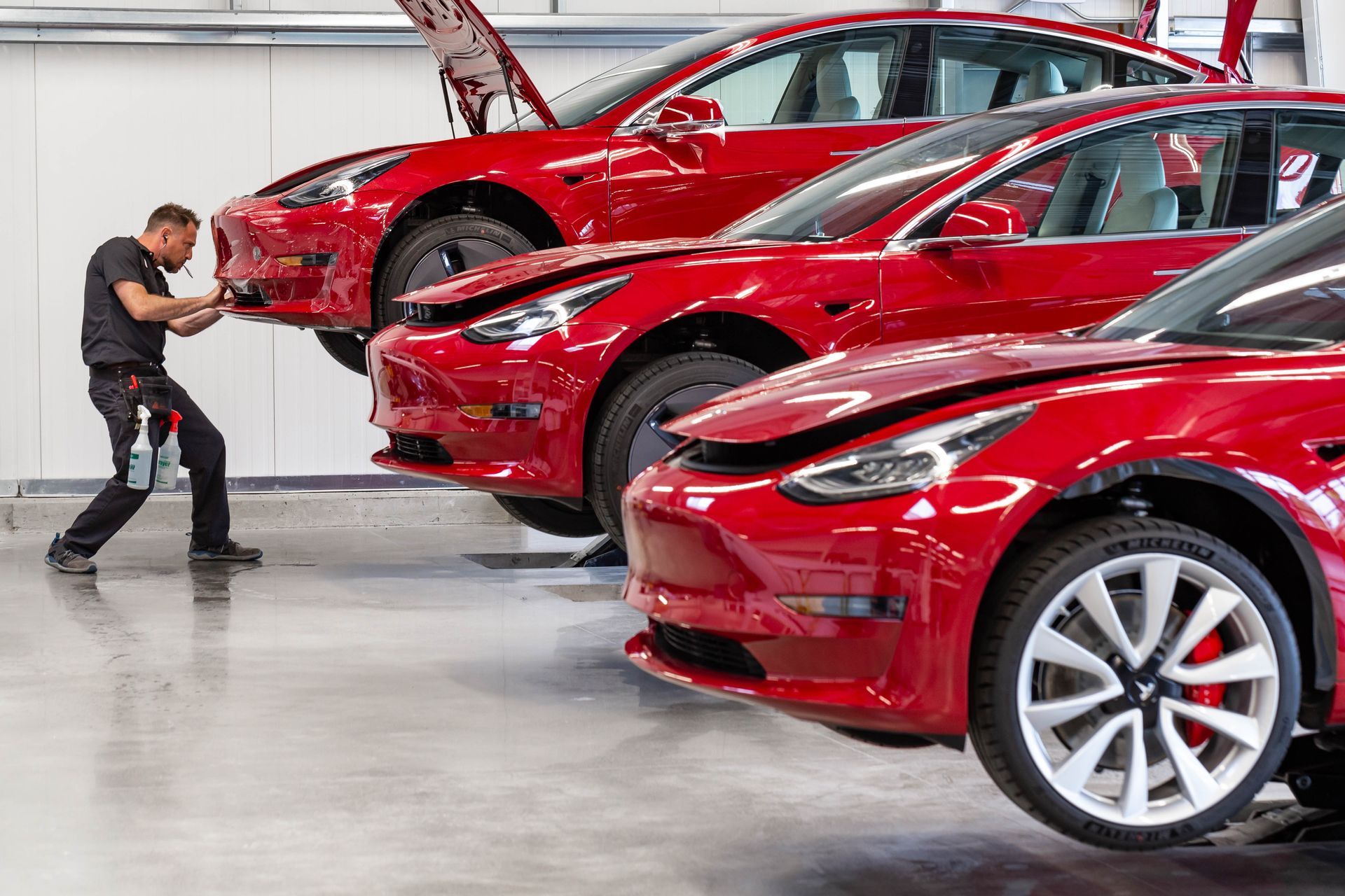 Red sports cars in an auto factory, with a worker inspecting the front car on the assembly line.