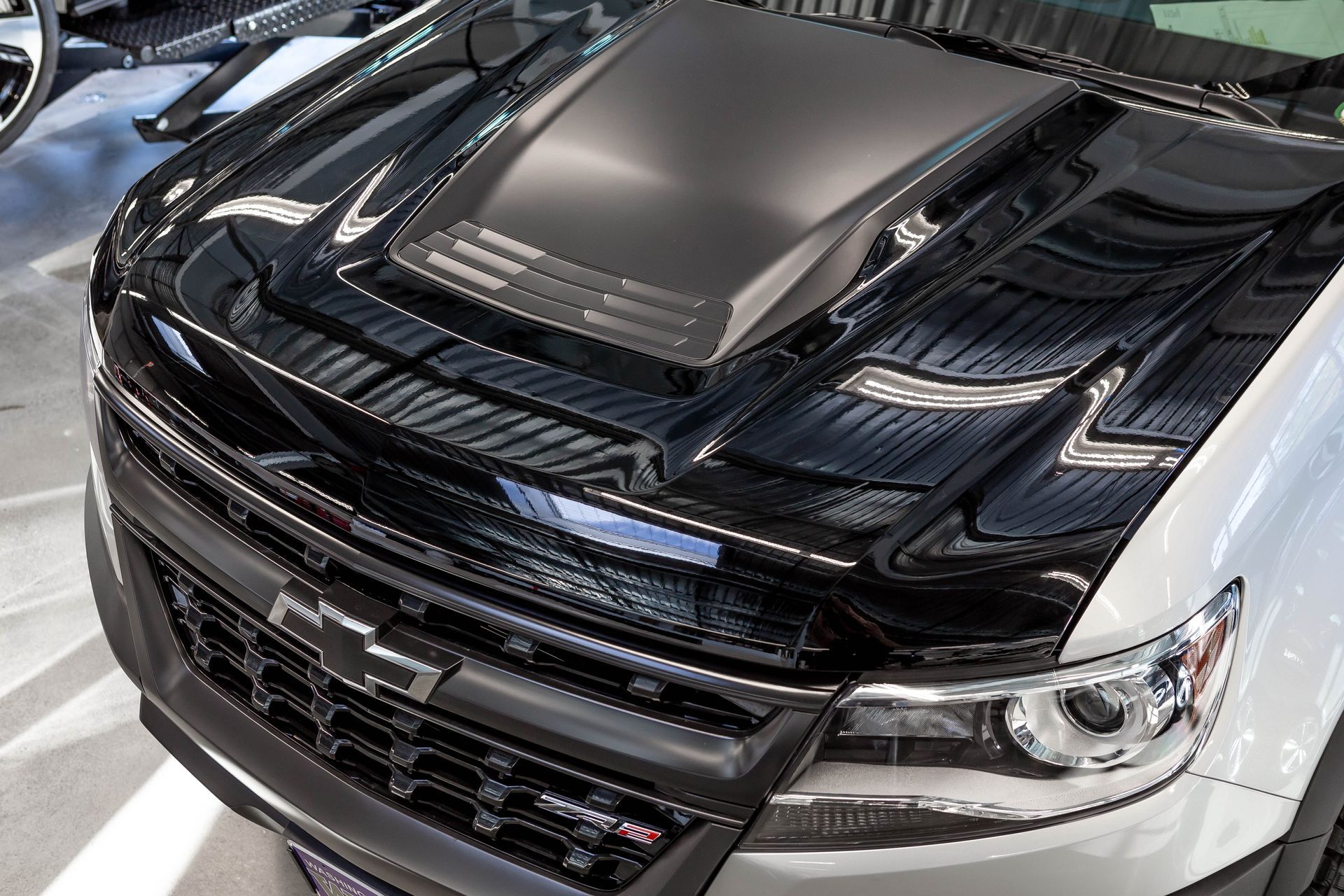 Close-up of a black and silver sports car front grille and hood in a garage or showroom