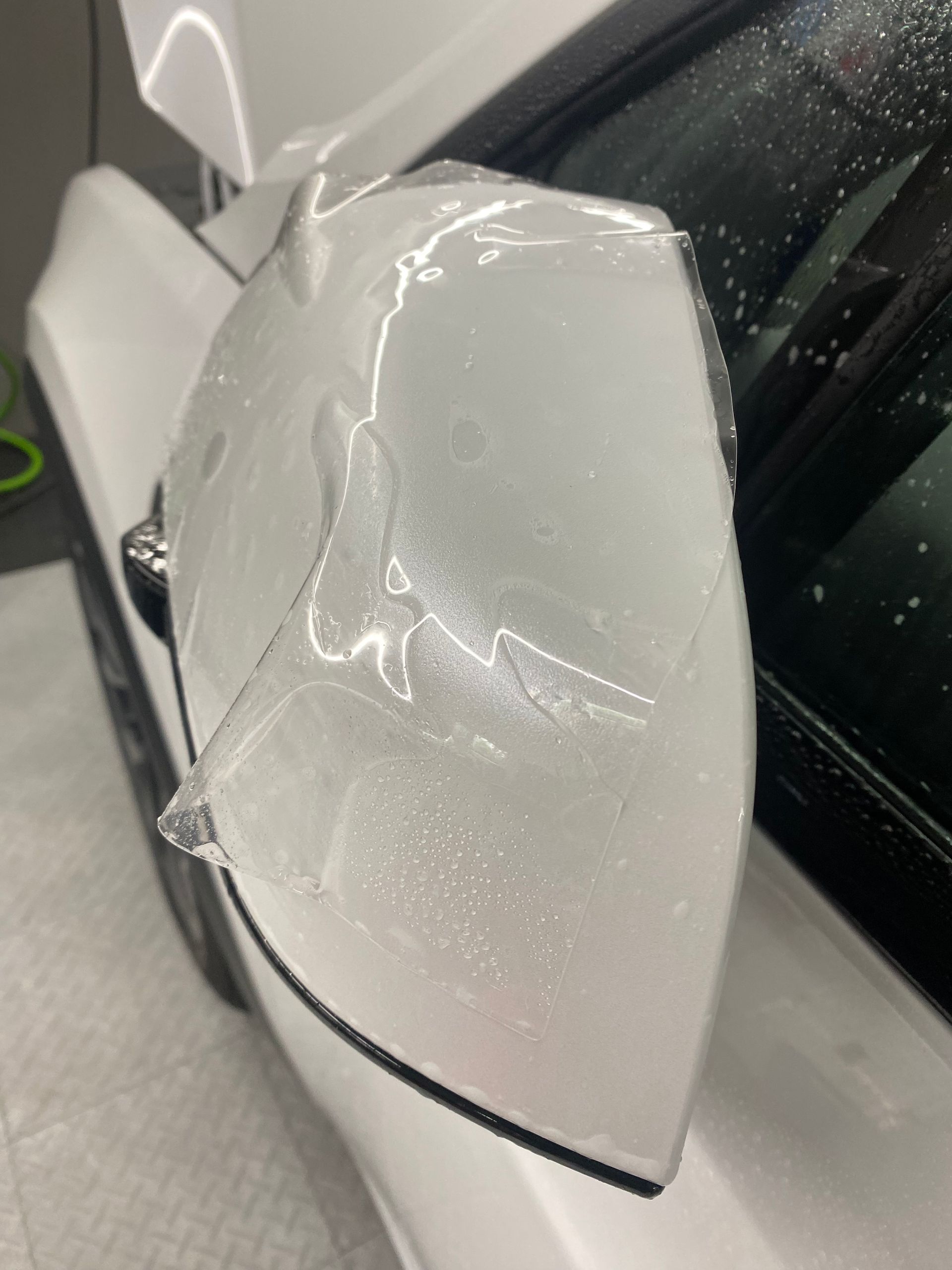 Close-up of a damaged white car side mirror with cracked housing and torn cover.