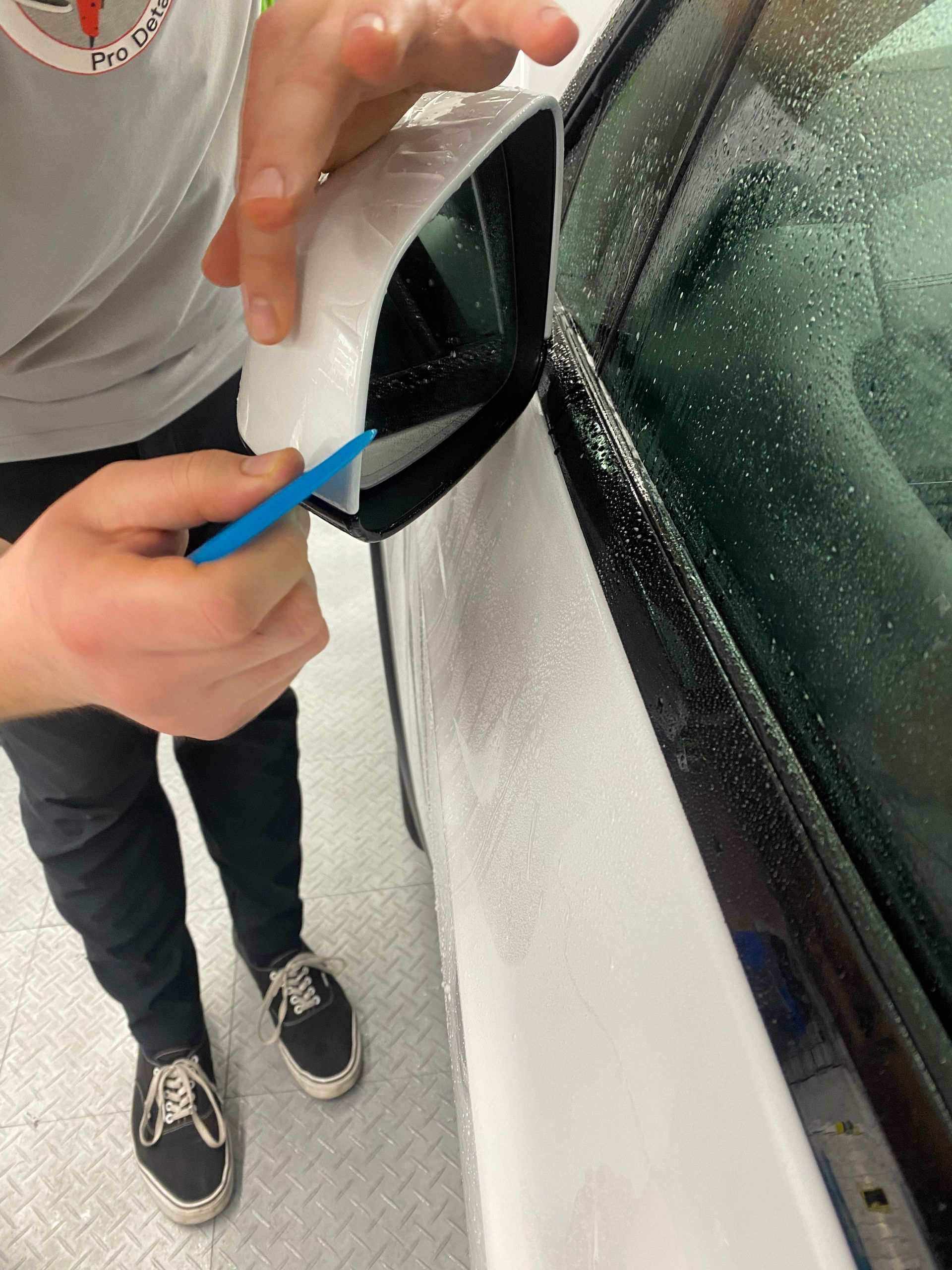 Person using a blue tool to pry a black trim piece from a white car window.