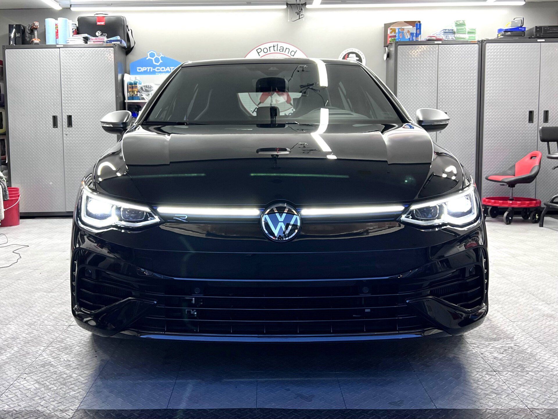 Black Volkswagen Golf R parked inside a garage, illuminated headlights, chrome badge, and reflective floor.
